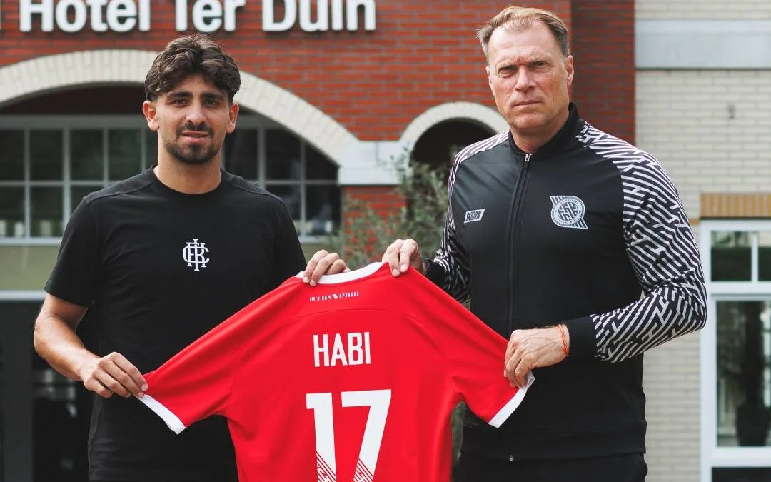 Два мужчины держат красную футболку игрока HABI с номером 17
