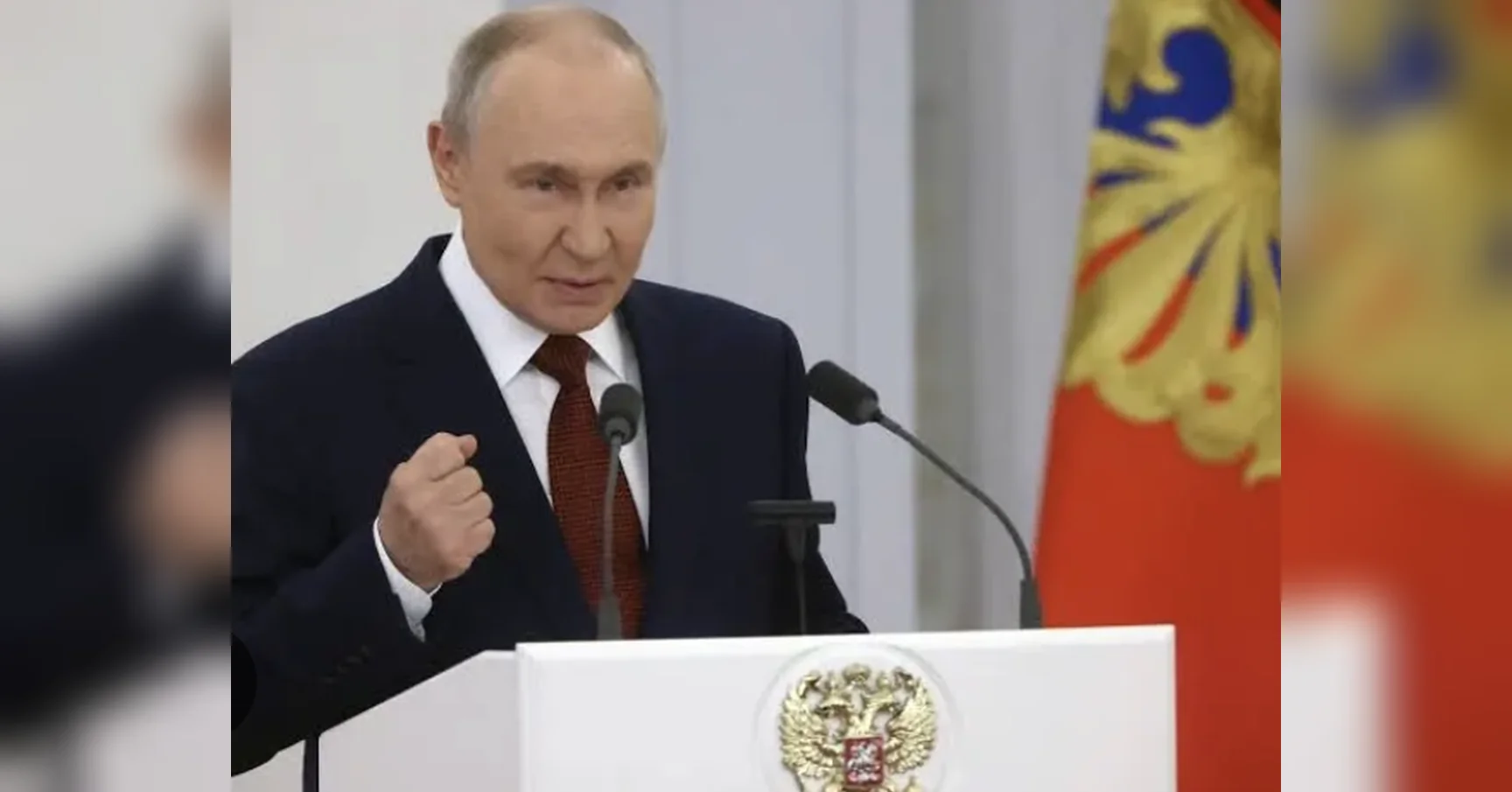 Володимир Путін виступає за білою трибуною з гербом Росії, стиснувши кулак