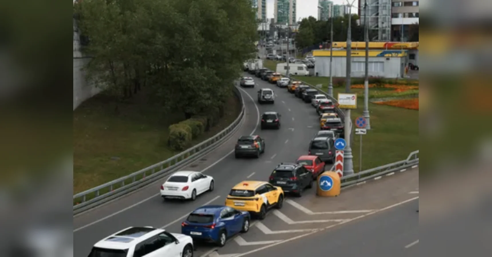 Довга черга легкових авто на вигнутій міській дорозі біля заправки