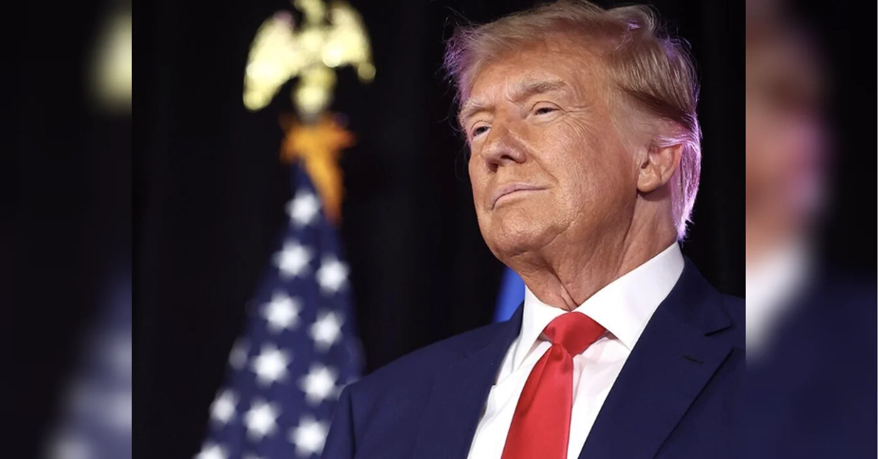 Дональд Трамп у синьому костюмі з червоною краваткою на тлі прапора США