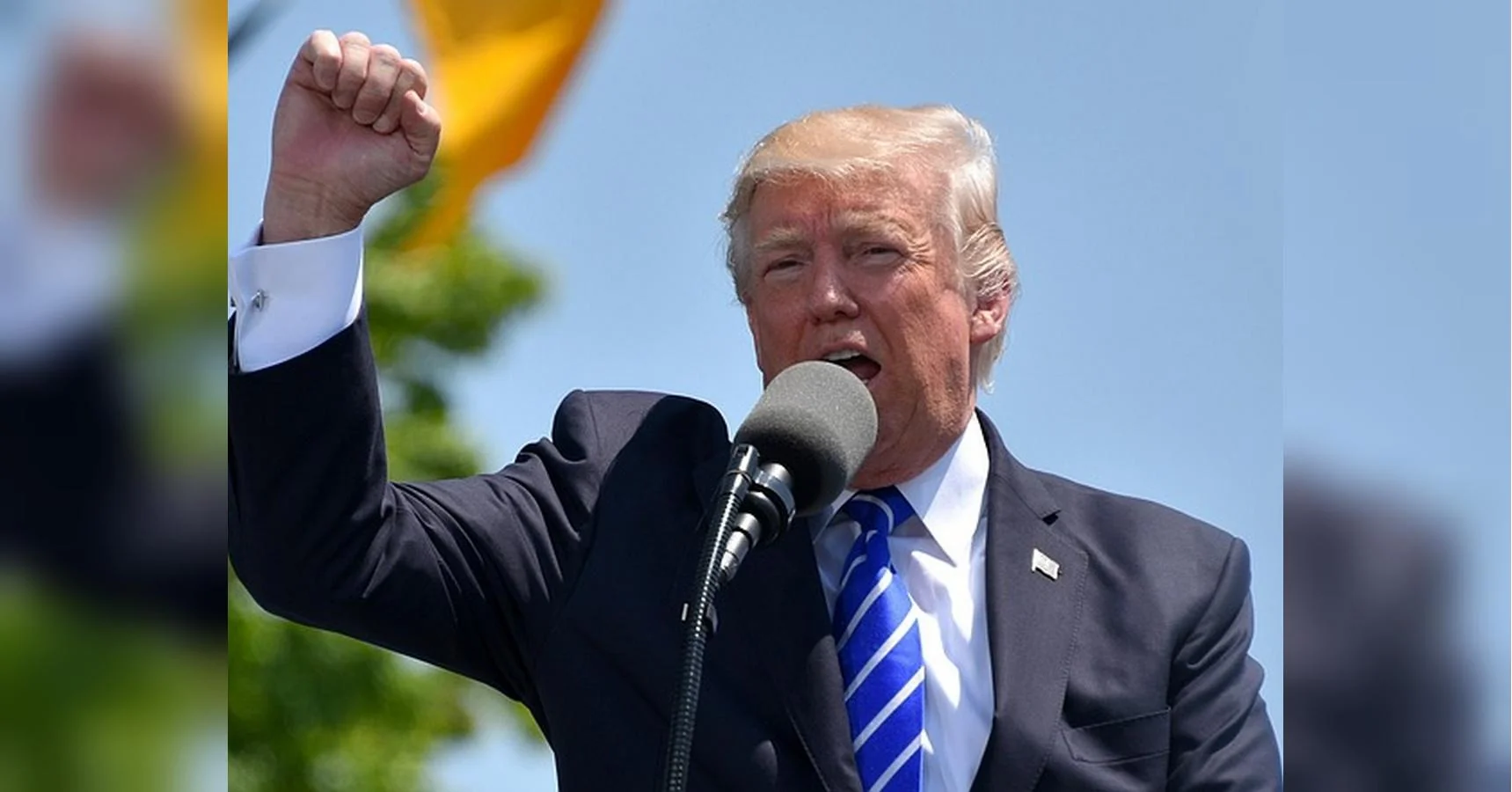 Дональд Трамп у костюмі виступає з піднятим кулаком біля мікрофона