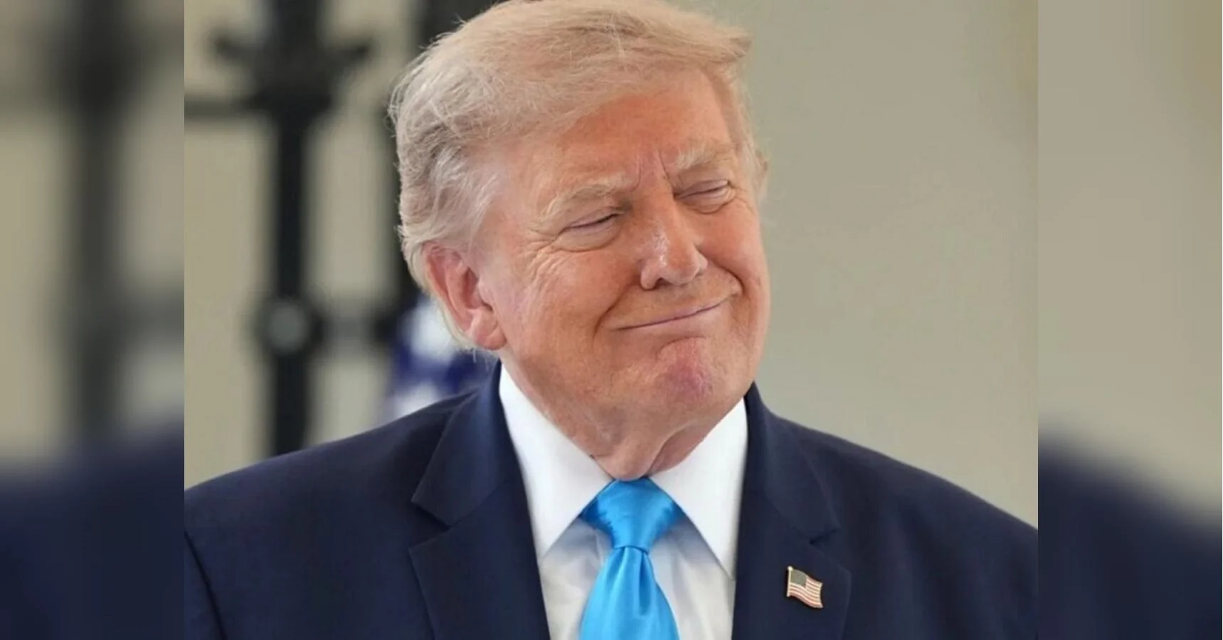 Дональд Трамп у темно-синьому костюмі з блакитною краваткою посміхається із заплющеними очима