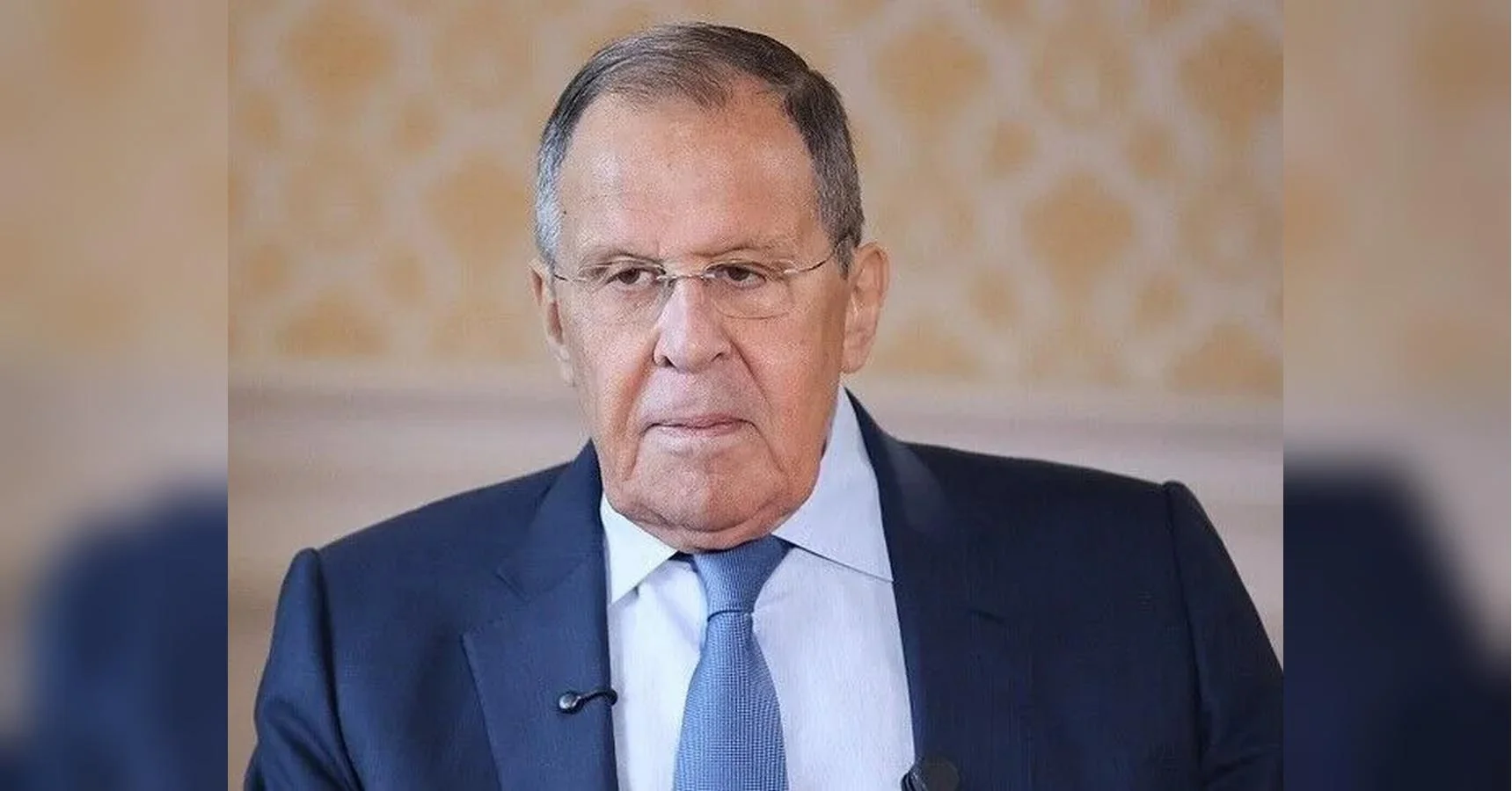 Сергій Лавров у темному костюмі з блакитною краваткою та мікрофоном