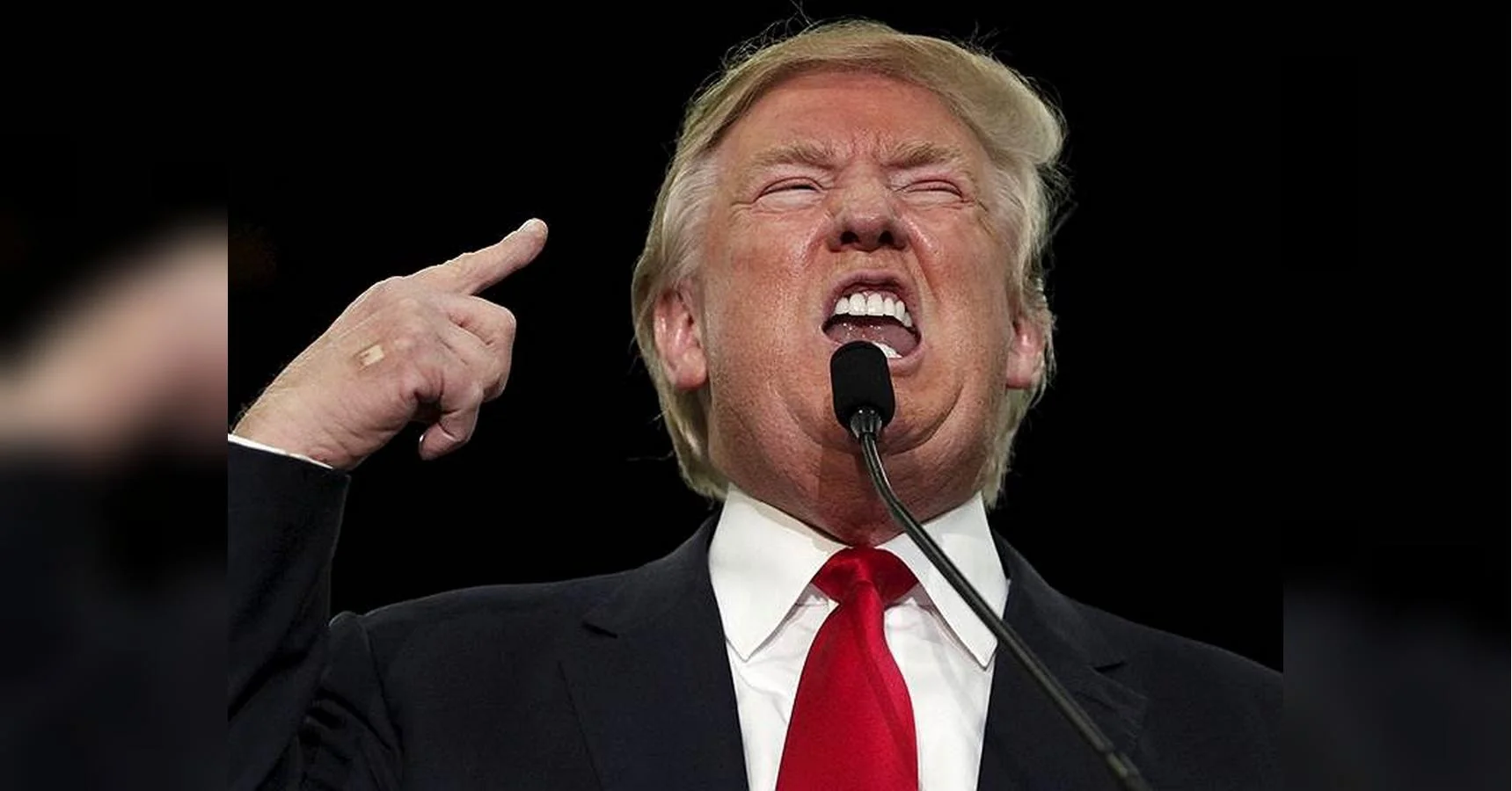 Дональд Трамп у костюмі з червоною краваткою говорить у мікрофон