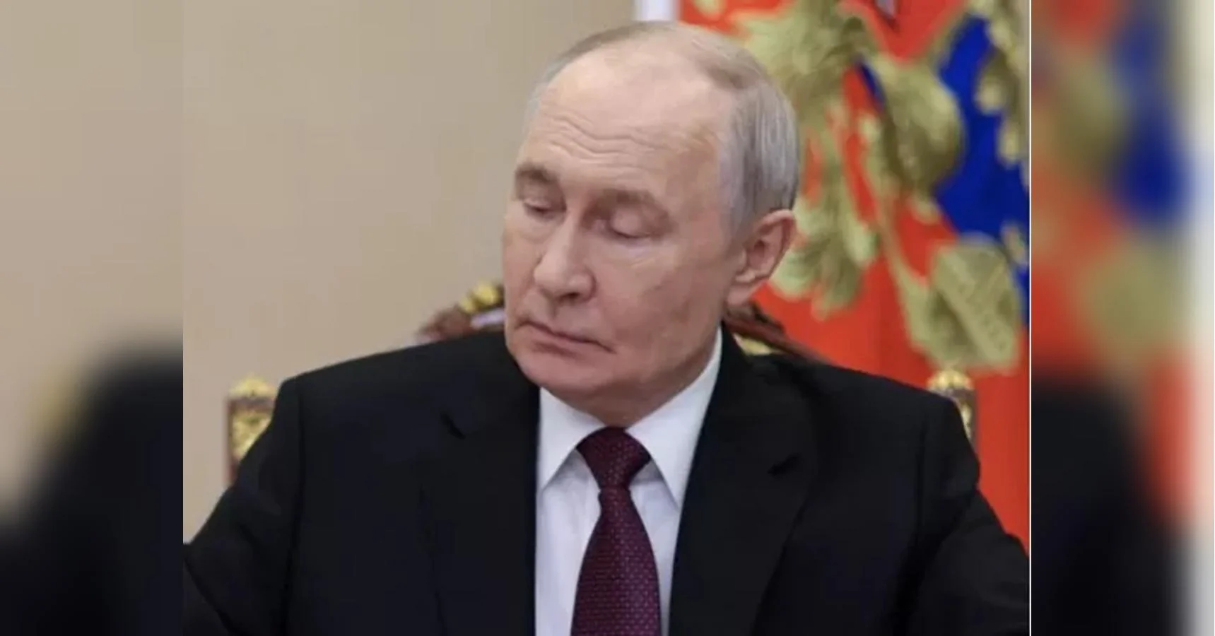 Володимир Путін у костюмі сидить на тлі президентського штандарта