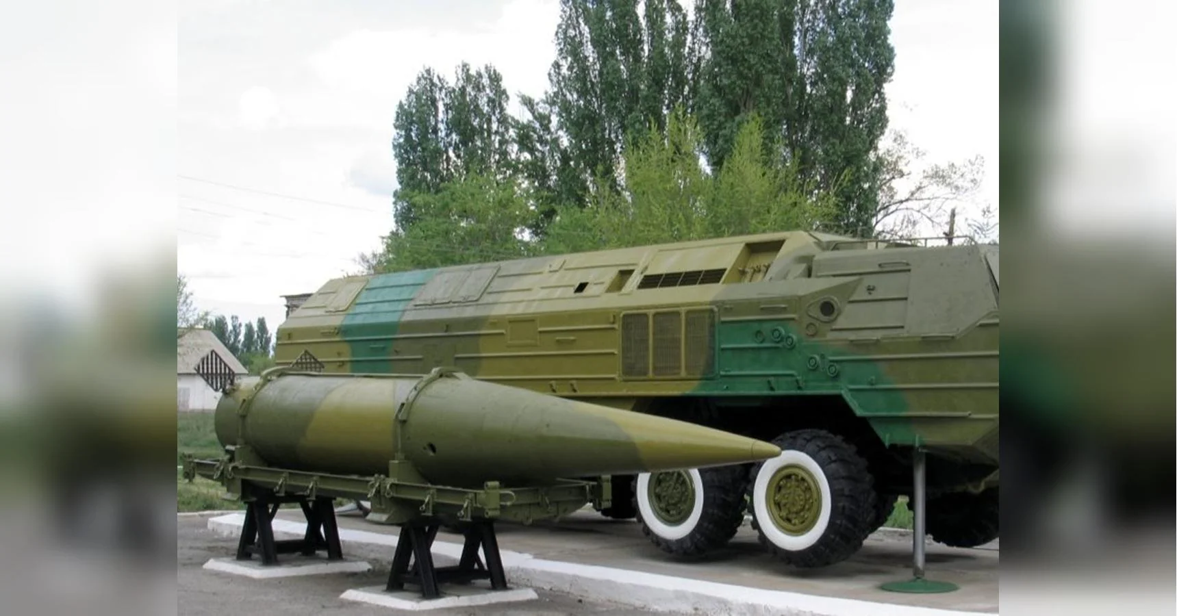 Зелена колісна пускова установка і балістична ракета на стенді біля дерев