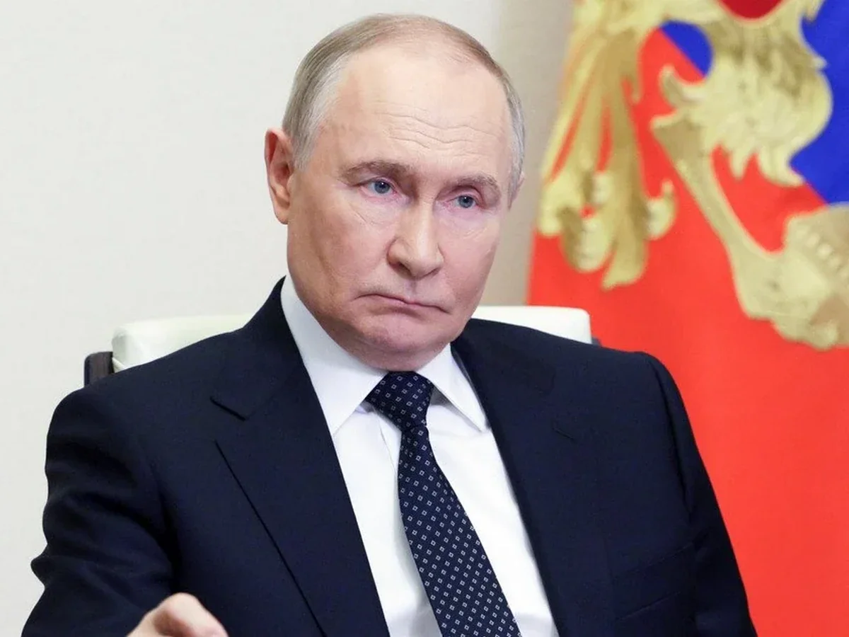 Володимир Путін у темному костюмі сидить біля президентського прапора Росії