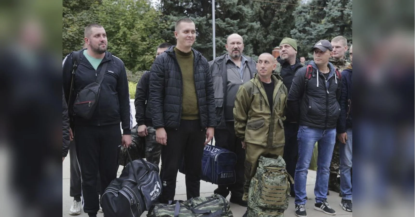 Чоловіки з дорожніми сумками та рюкзаками стоять групою на вулиці