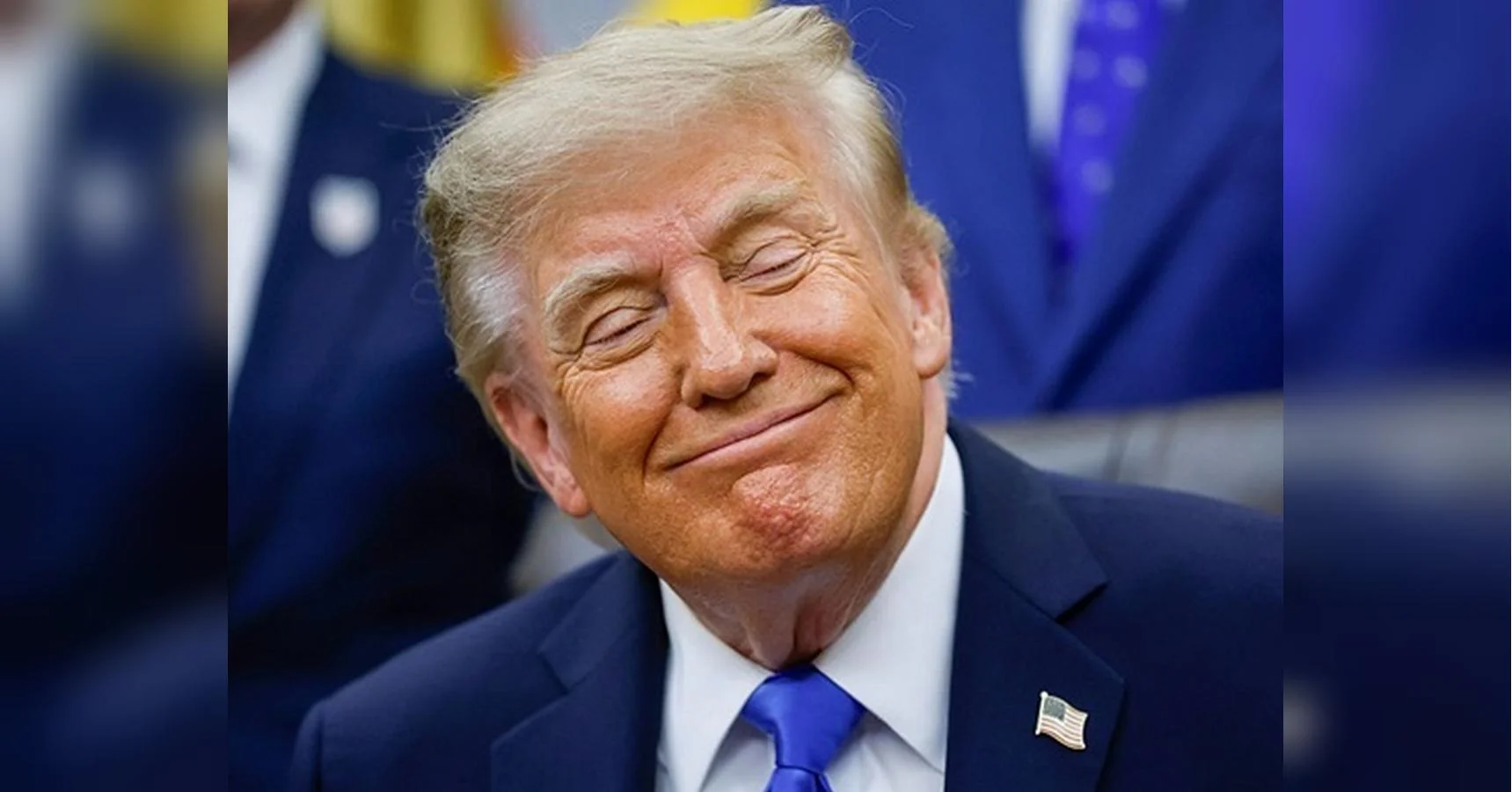Дональд Трамп усміхається із заплющеними очима в темно-синьому костюмі з прапорцем США